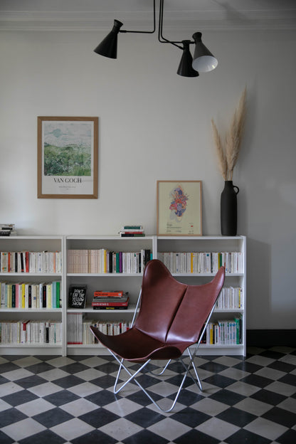 Fauteuil Papillon Cuir bordeau - Structure inox - Vue de 3/4 dans une bibliothèque