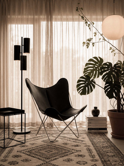 Fauteuil Papillon Cuir noir - Structure inox - Vue de 3/4 sur un tapis de salon