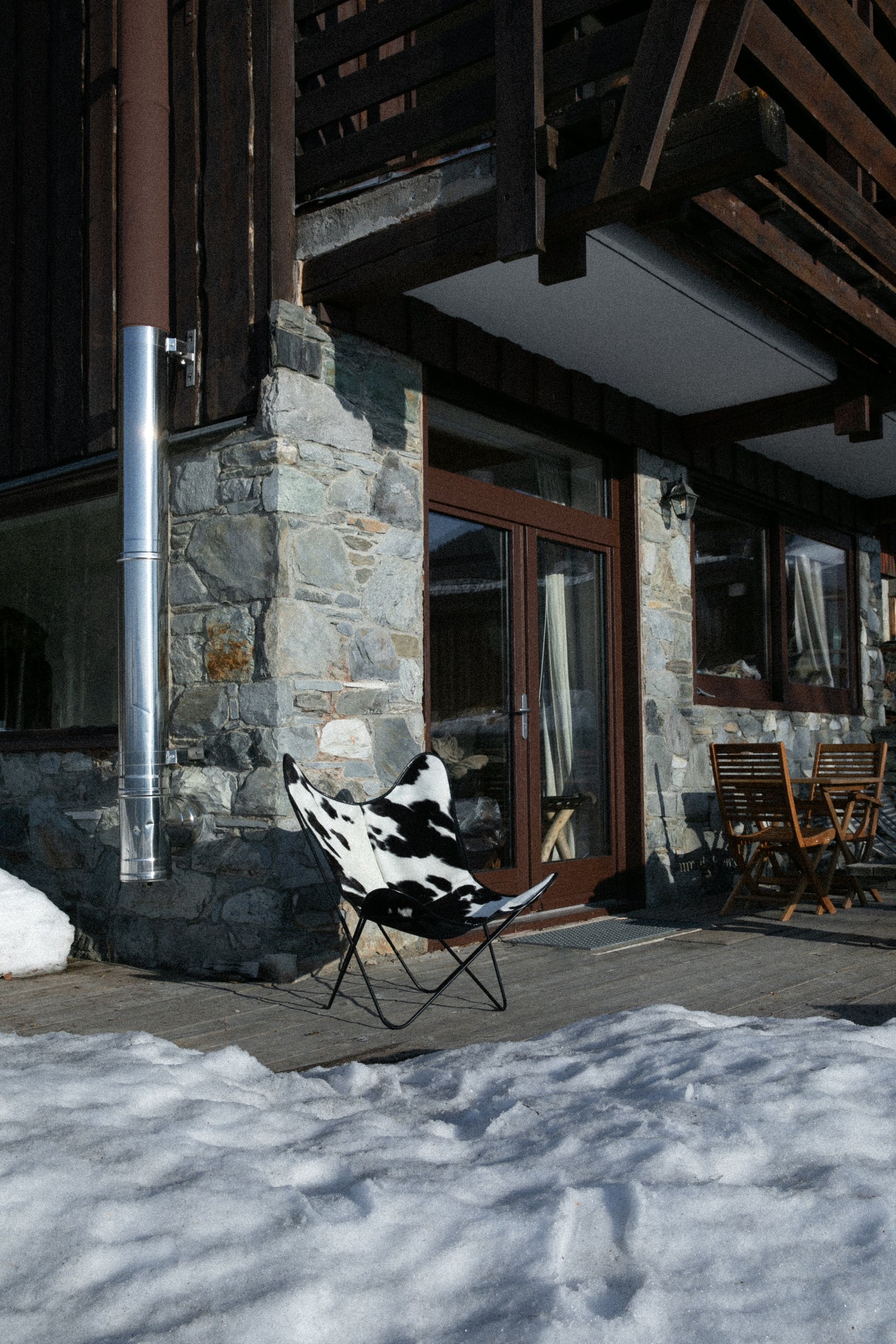 Fauteuil Papillon Cuir Vache Noire -  Structure Noire - Vue de 3/4 au pied d'un chalet de montagne