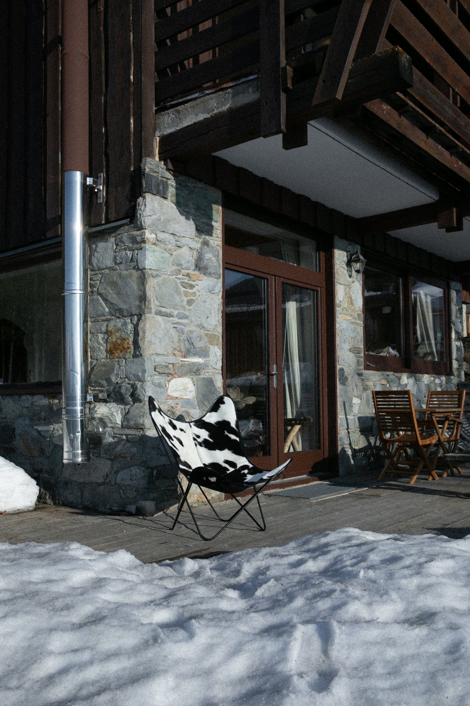 Fauteuil Papillon Cuir Vache Noire -  Structure Noire - Vue de 3/4 au pied d'un chalet de montagne