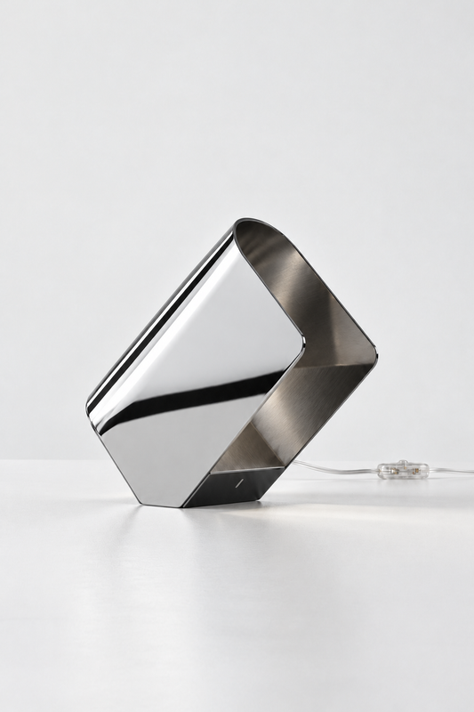 Lampe à poser design PLIS chrome en position inclinée, posée sur l’angle, lumière rasante
